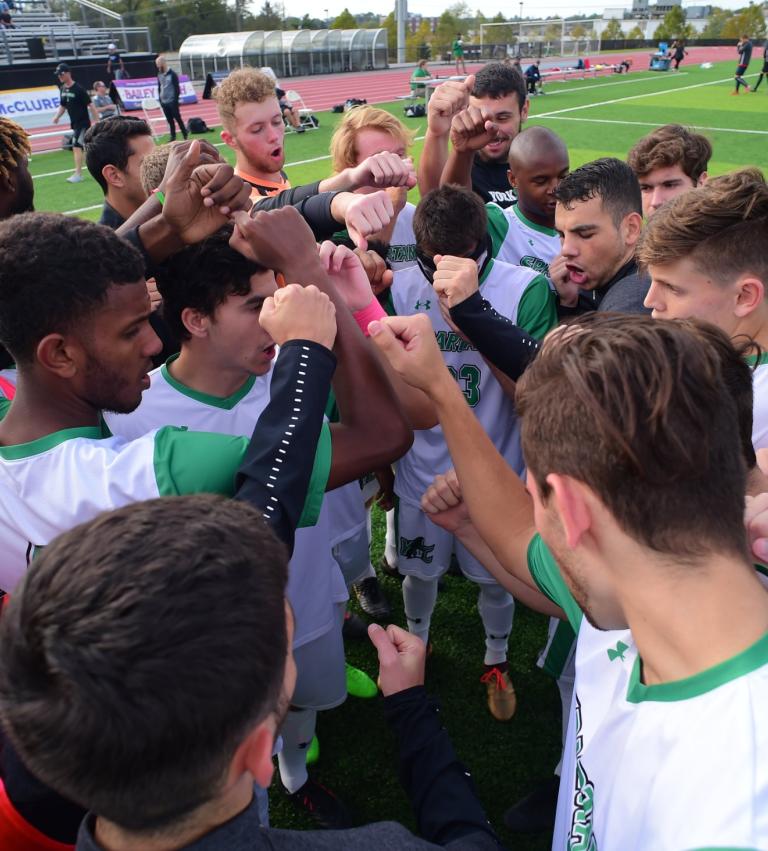 York student-athletes huddle together in a circle on campus field