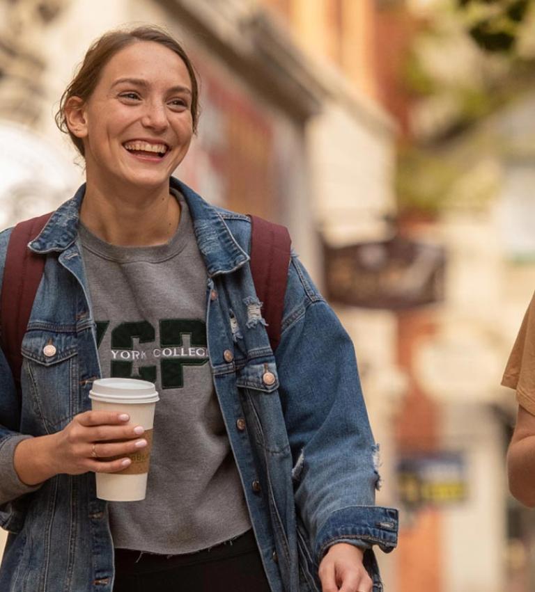 Two students walk through campus with coffees in their hands