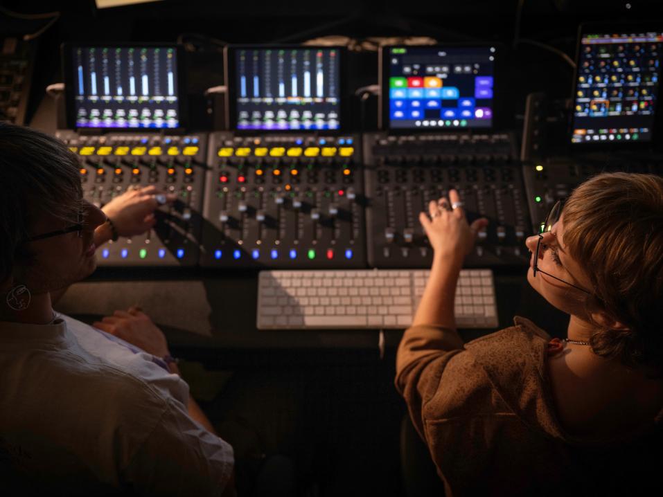 Students sit in front of a music recording studio control panel.