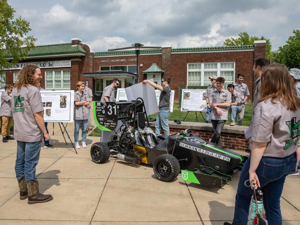 A group of students surround a racecar outside the Kinsley Engineering Center