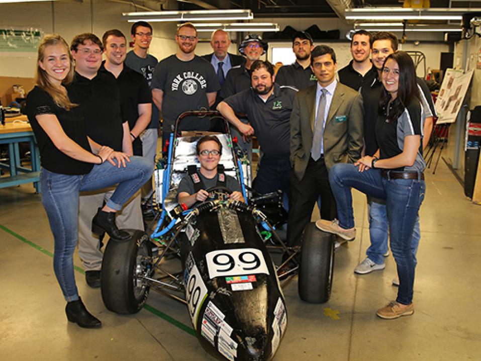 A group of YCP engineering students stand around their electric Formula SAE car in the engineering center; one student sits in the driver's seat.