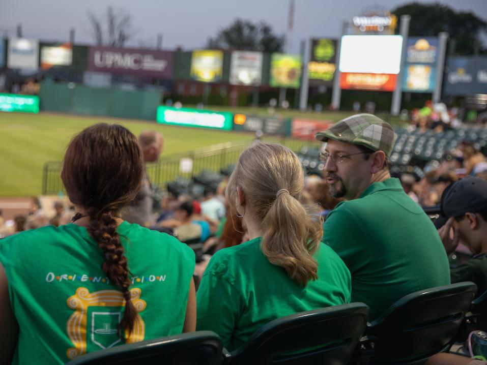 Three people dressed in York College green sit in the crowd at Rev's Stadium, enjoying a minor league baseball game in York.