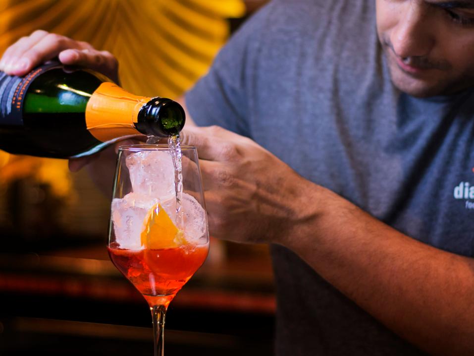 A mixologist pours a spirit into a class, making a colorful cocktail.