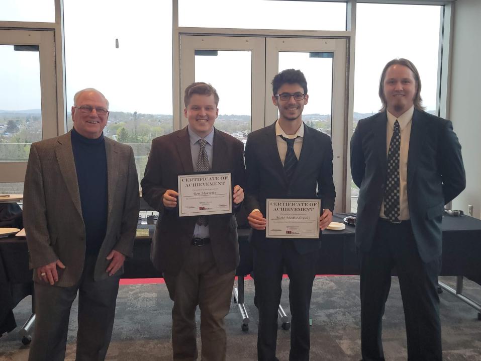 Four people smiling at the camera, two of them holding certificates