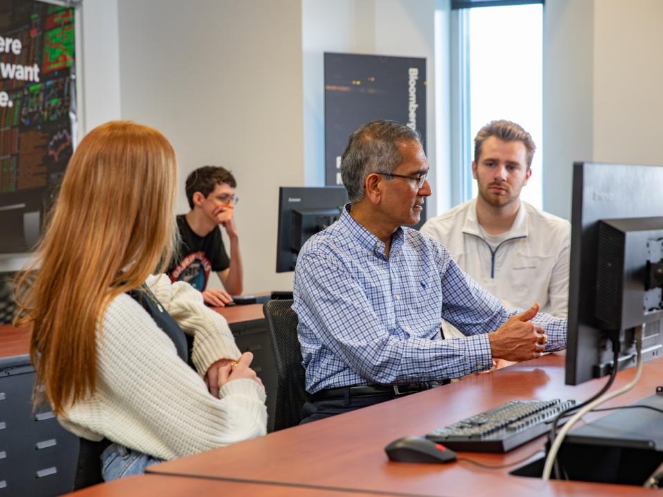 Instructor talking with students in a computer lab classroom.