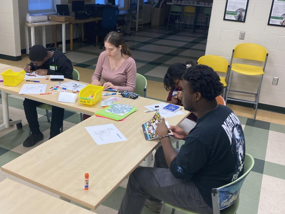 Tavon Cornish sits at a desk with three other people working on a craft