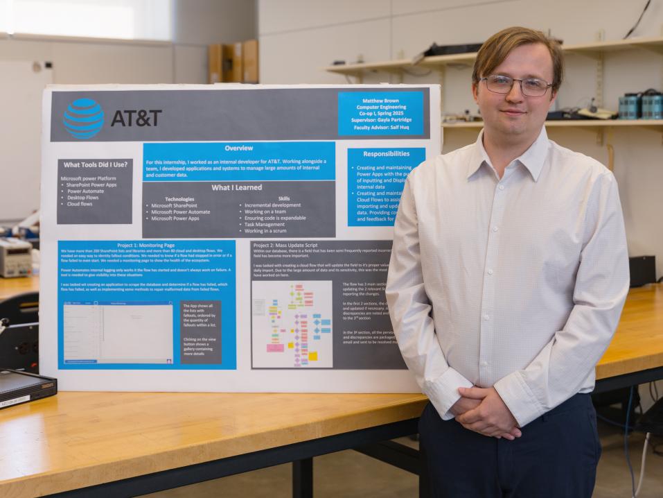 A student stands next to his poster presentation in a classroom.