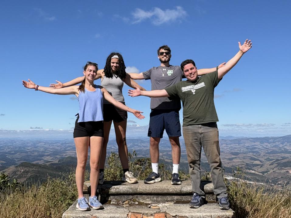 A group of students on a mountain top in Brazil with their arms raised.