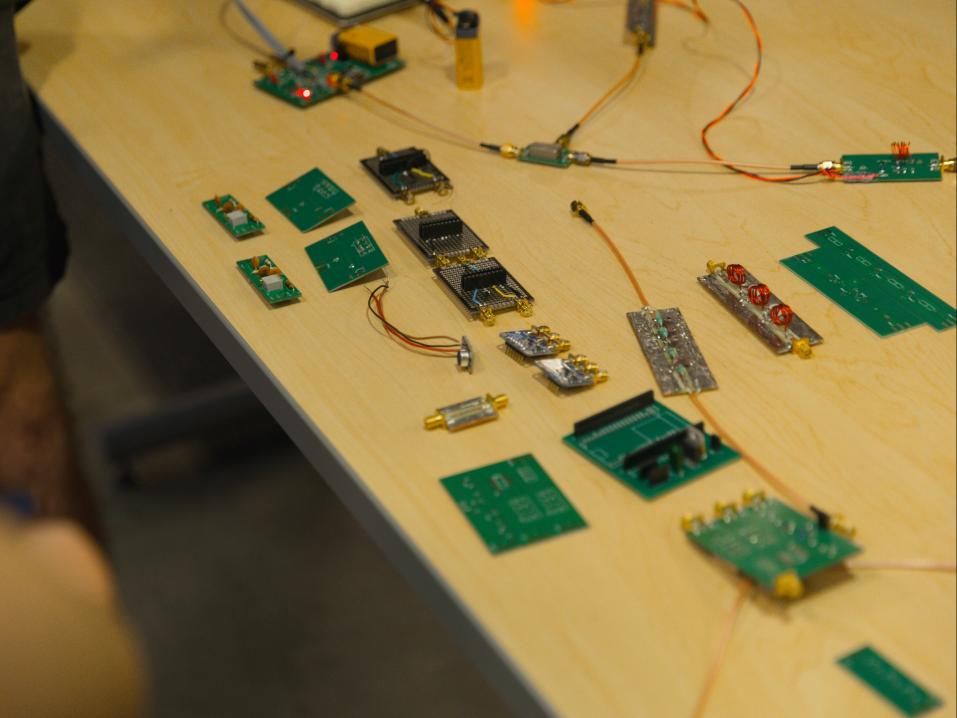 A tabletop covered with various electronic circuit boards, modules, cables, connectors, and other hardware components.