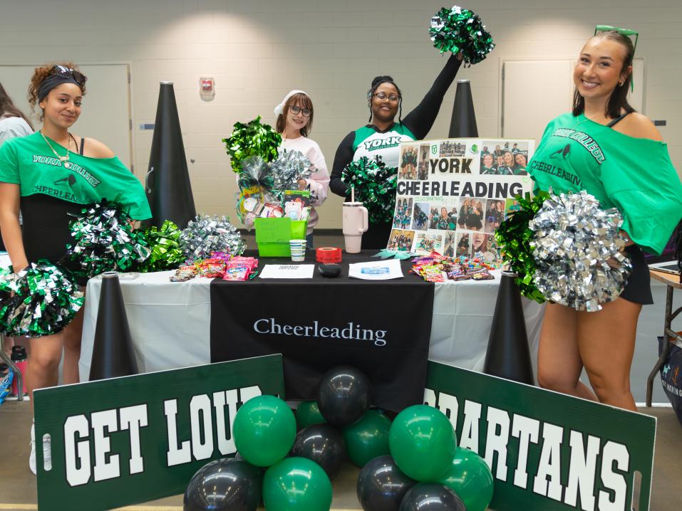 Cheerleaders with pom poms at the Involvement fair surrounded by signs and balloons.