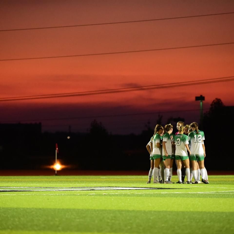 Group of athletes huddled on the field to discuss strategy as the sun sets in the background