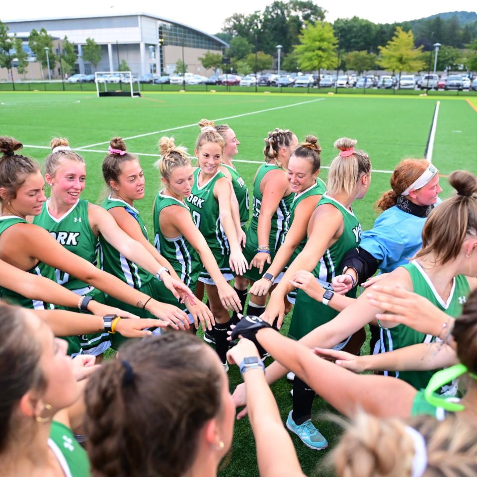 Women's field hockey players huddle and put their hands together on field