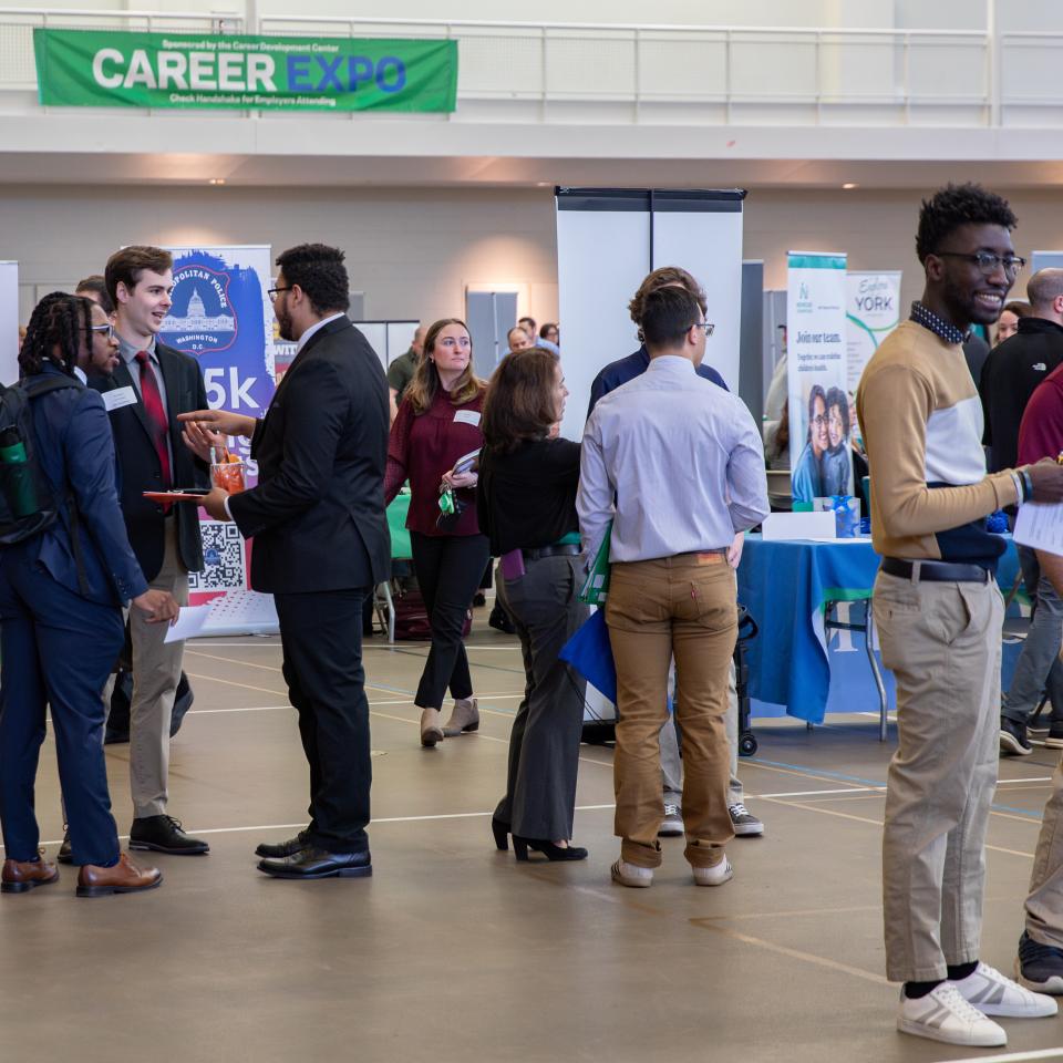 Individuals mingling at the YCP Career Expo. A large green banner is visible in the background.