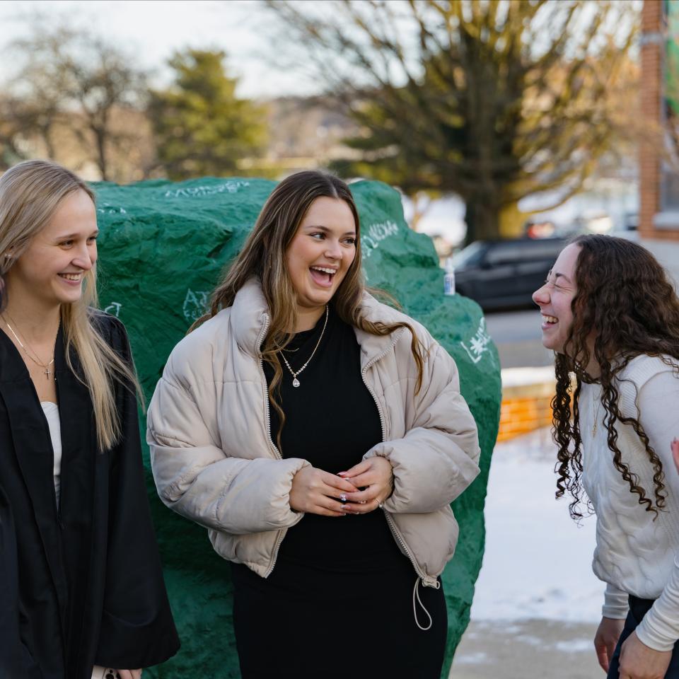 A group of graduating seniors laugh and talk at the rock