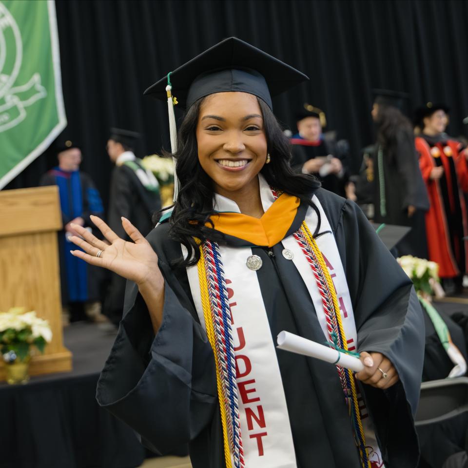A graduating senior waves to the camera in her cap and gown