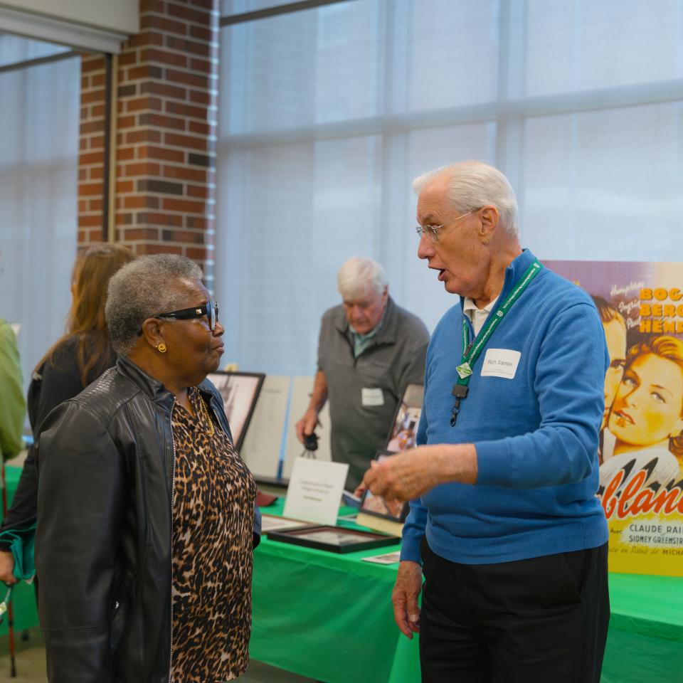 A man and a women stand talking in front of a table with old movie posters.