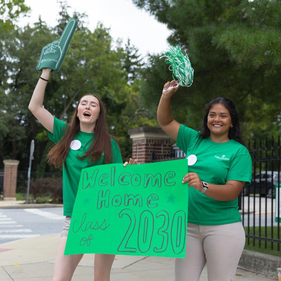 Two students hold foam fingers and welcome signs.
