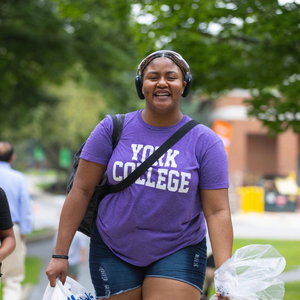 A student in a purple York College shirt walks outside.