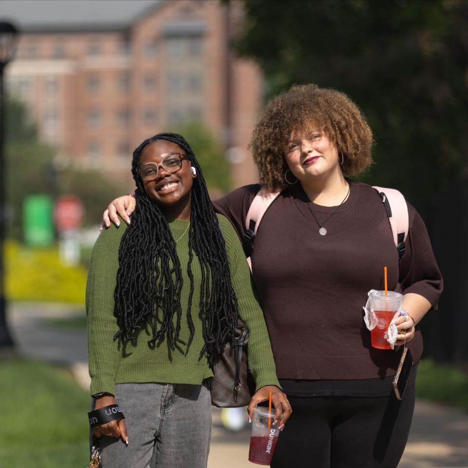 Two students stand together with the brick building of Northside Commons behind them.