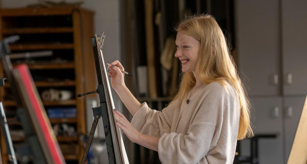 A student paints at an easel in an art studio classroom.