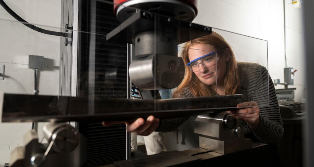 A student works with a machine in the engineering lab, wearing safety goggles.