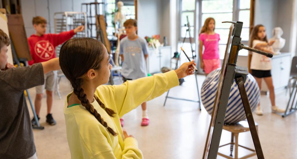 Students hold up their pencils to see the size of objects in a drawing class