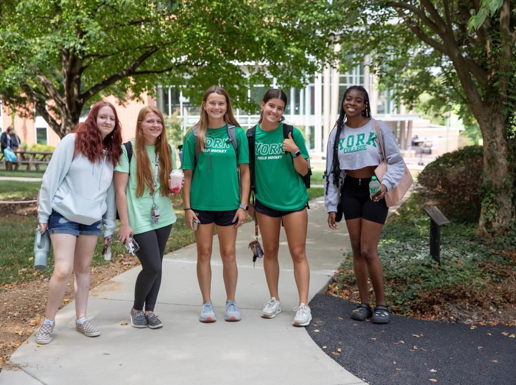 A group of students pose for the camera on the sidewalk near the library.