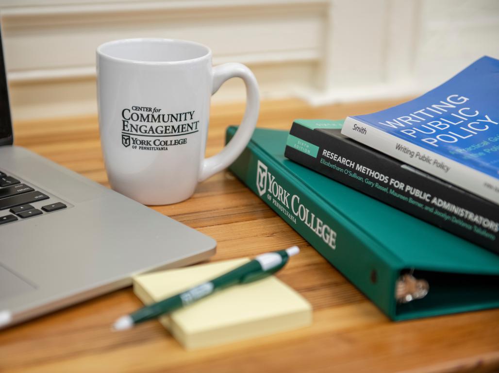 A Center for Community Engagement mug with 3 public policy books on the right side.