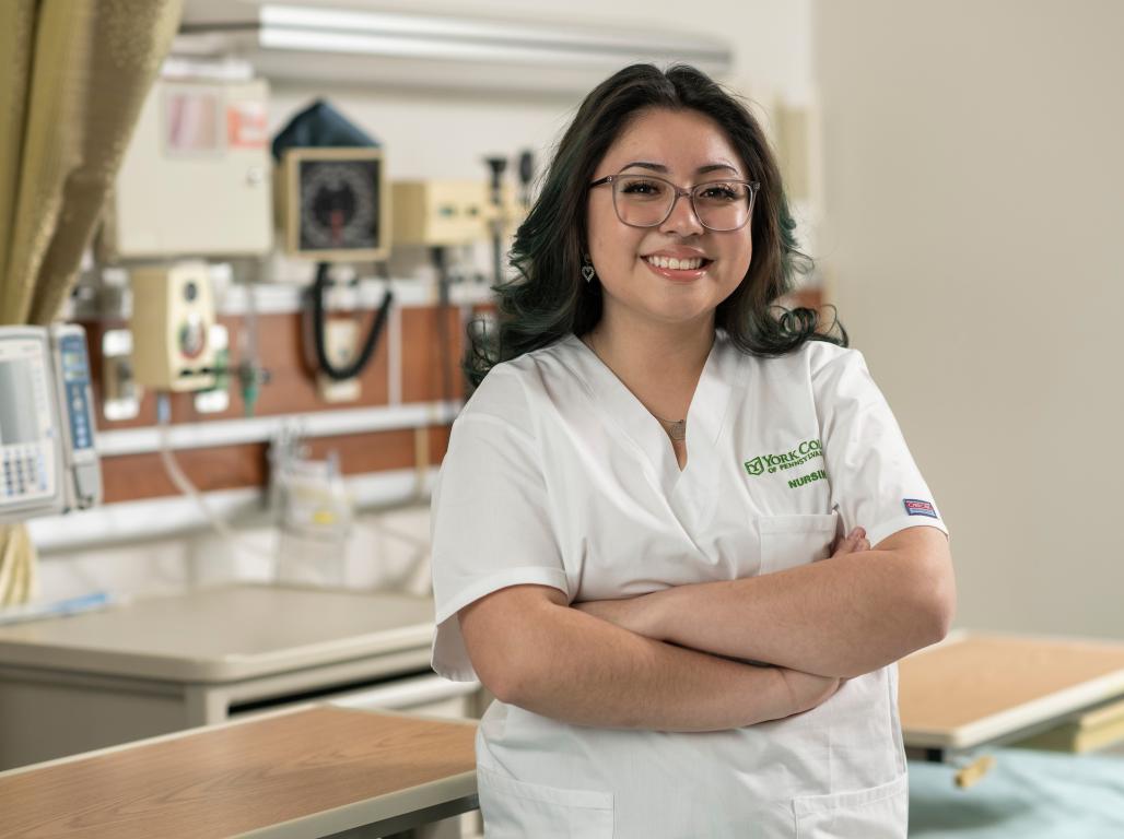 Maria Cruz poses for a photo in the nursing simulation lab as she wears her nursing scrubs.