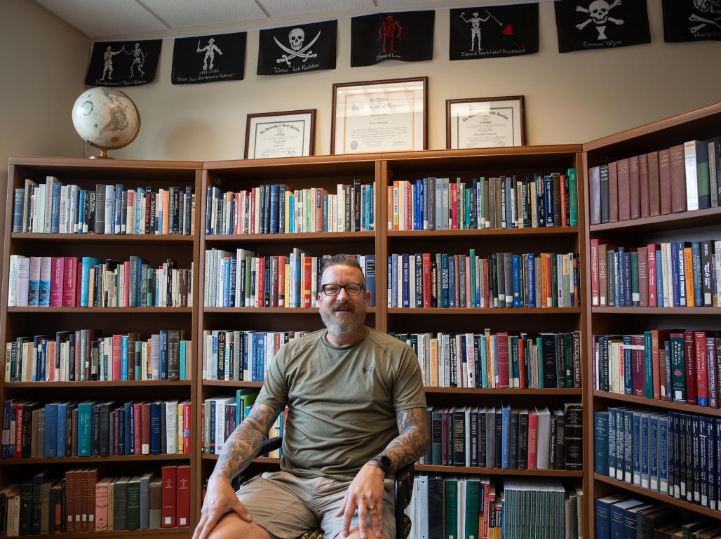 John Altman in his office space with bookshelves behind him.