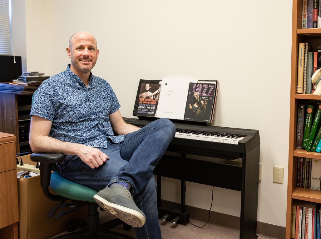 Ken Osowski sitting in his office next to a keyboard piano.