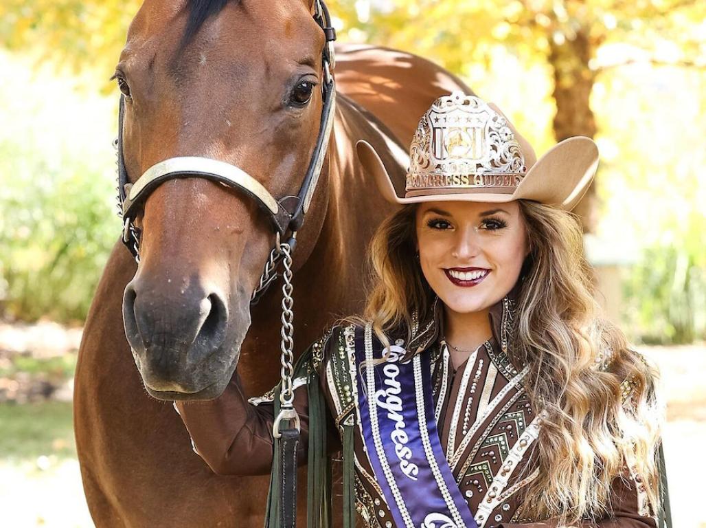 Kylie Good poses for a photo, dressed in western-style stress with a pageant sash across her chest. She stands beside her horse.