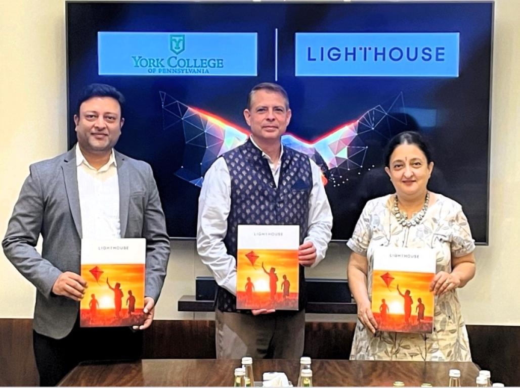 Three representatives of Lighthouse Learning pose behind a table holding program brochures.