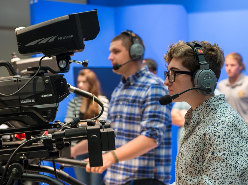 Students wearing headphones operate professional video cameras during a production. 