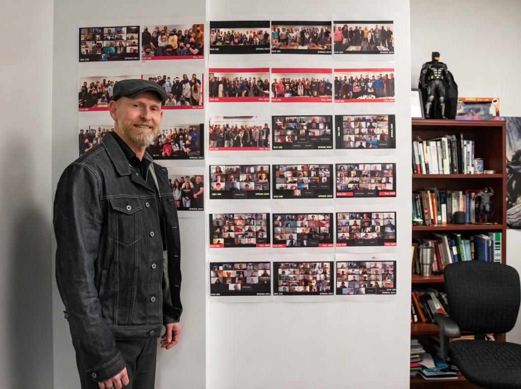 Matt Shatzkin stands in front of a wall of photographs. A shelf off to the side holds books and a Batman figurine.