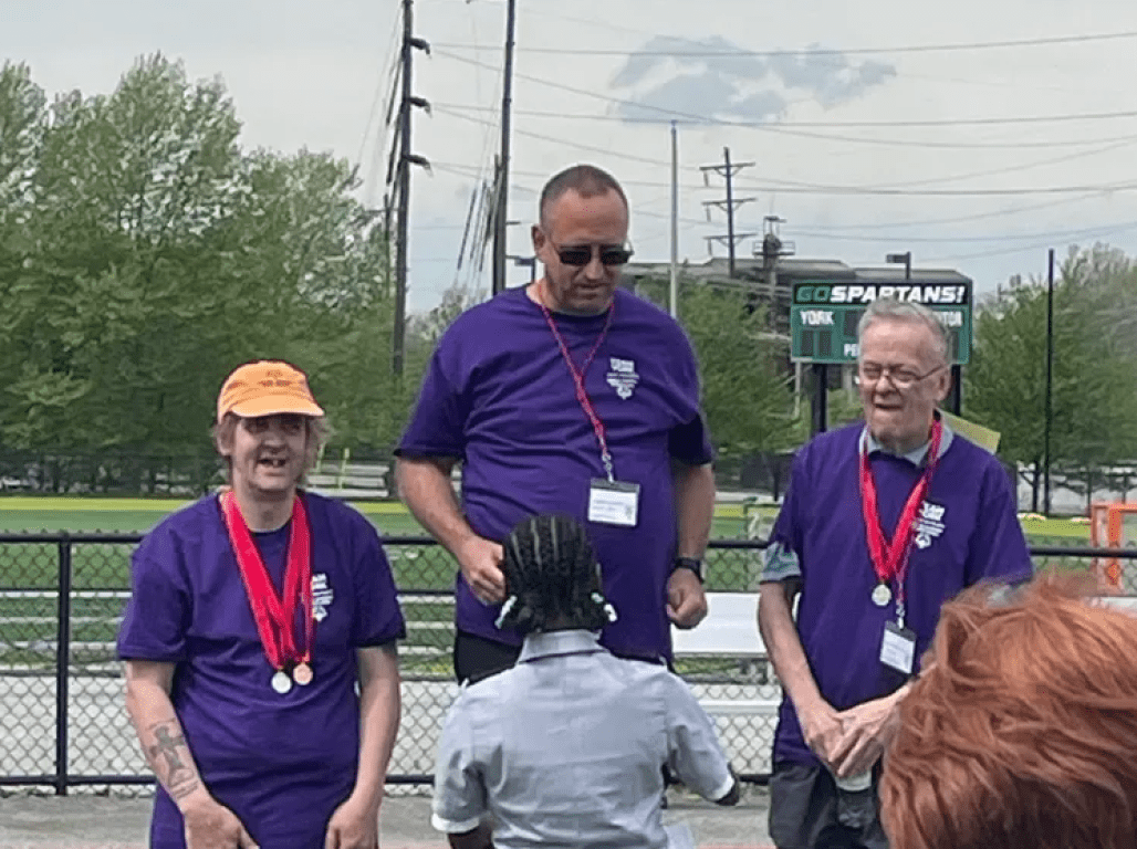 Three athletes accept medals at the podium during the Special Olympics ceremony at York College.