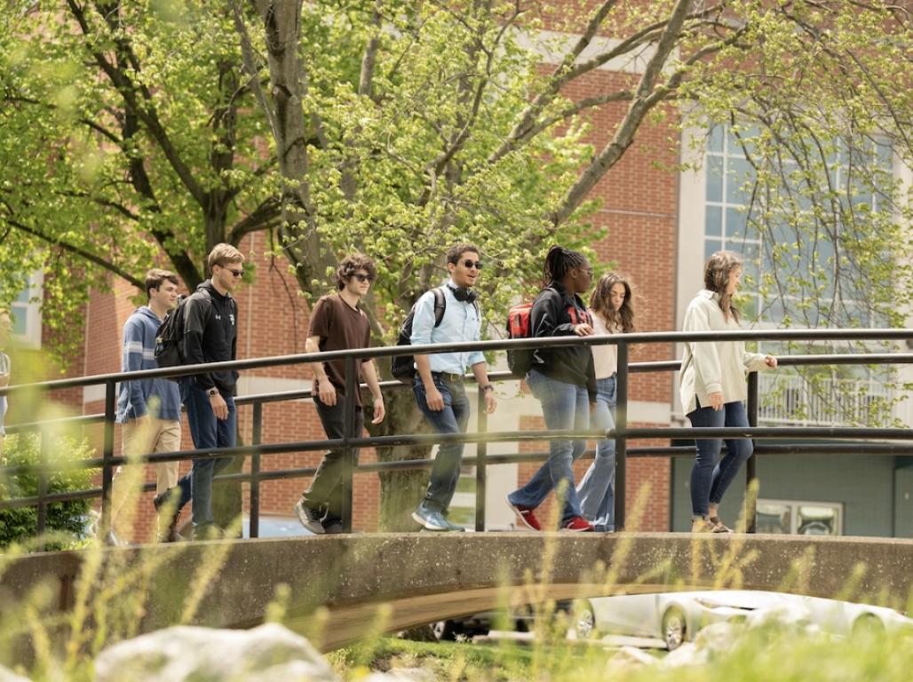A group of students walks across the campus creek bridge.