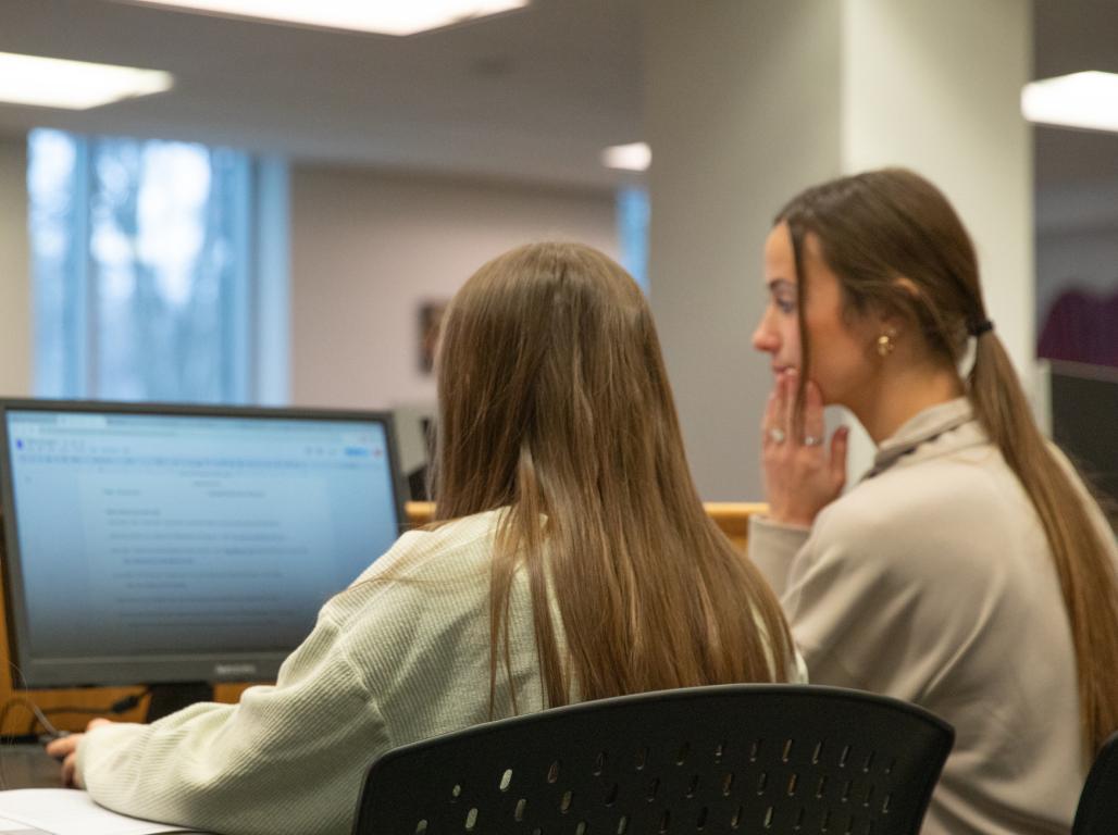 Three students sit at a computer in the York College library, looking at the screen together.