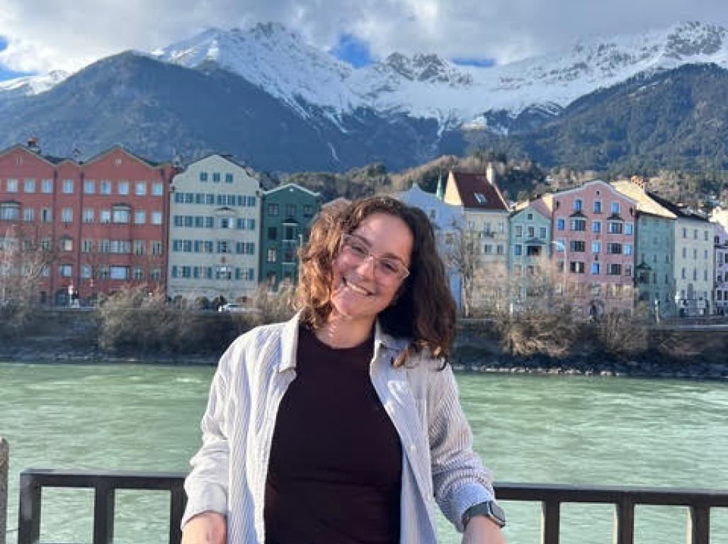 Gia Levis smiling in front of a scenic view of Innsbruck, Austria's mountains, houses, and a river.