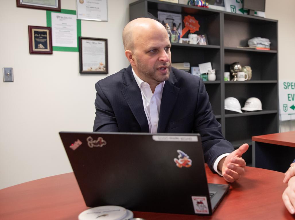 Jeff Vermeulen sitting at a desk with a computer speaking with a colleague.