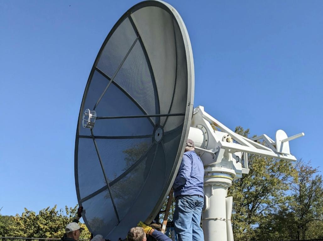 Three men holding the radio telescope, while a fourth man works on it from a ladder.