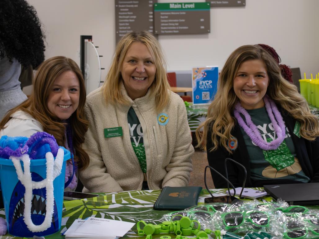 Three women sit at a table smiling at YCPGives event