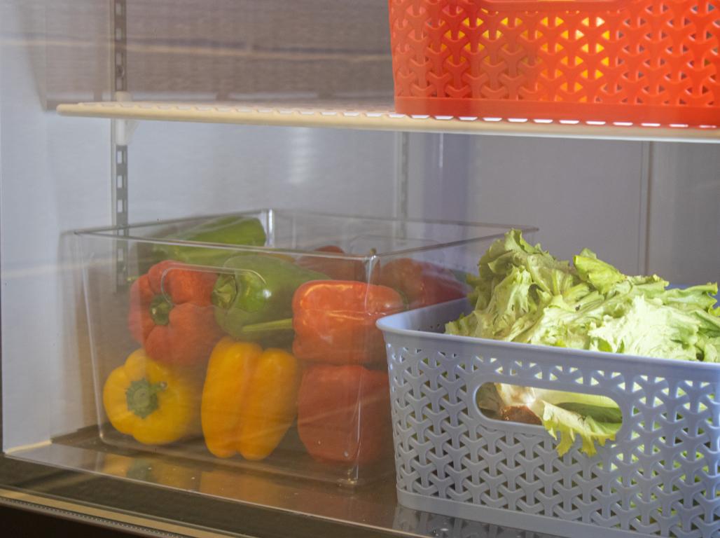 Several colors of bell peppers and fresh lettuce organized in plastic bins in a fridge.