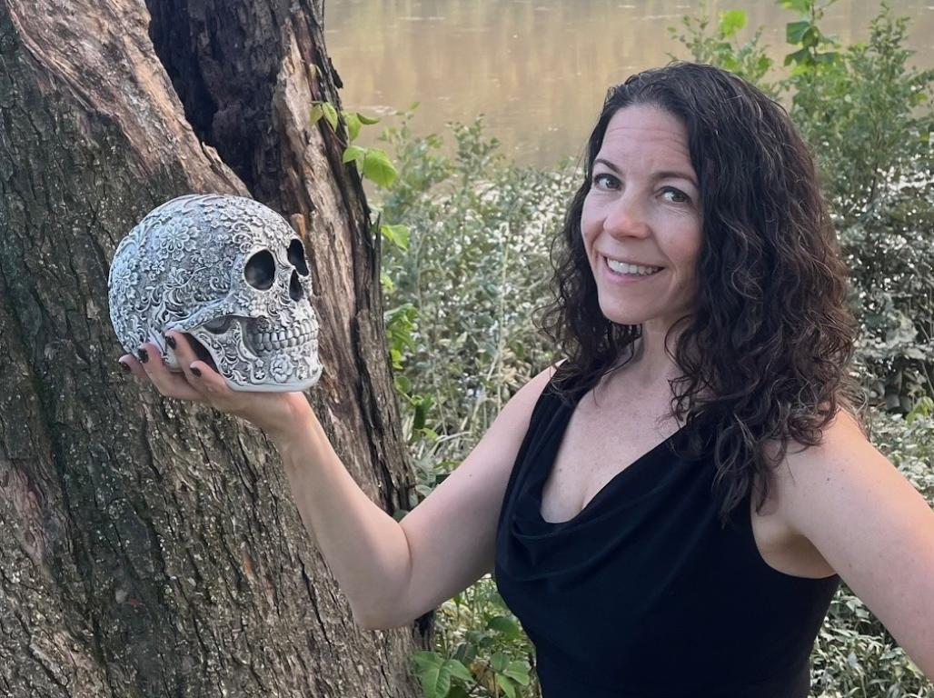 Dr. Cassandra O’Sullivan Sachar ‘99 posing with a skull in a wooded area.