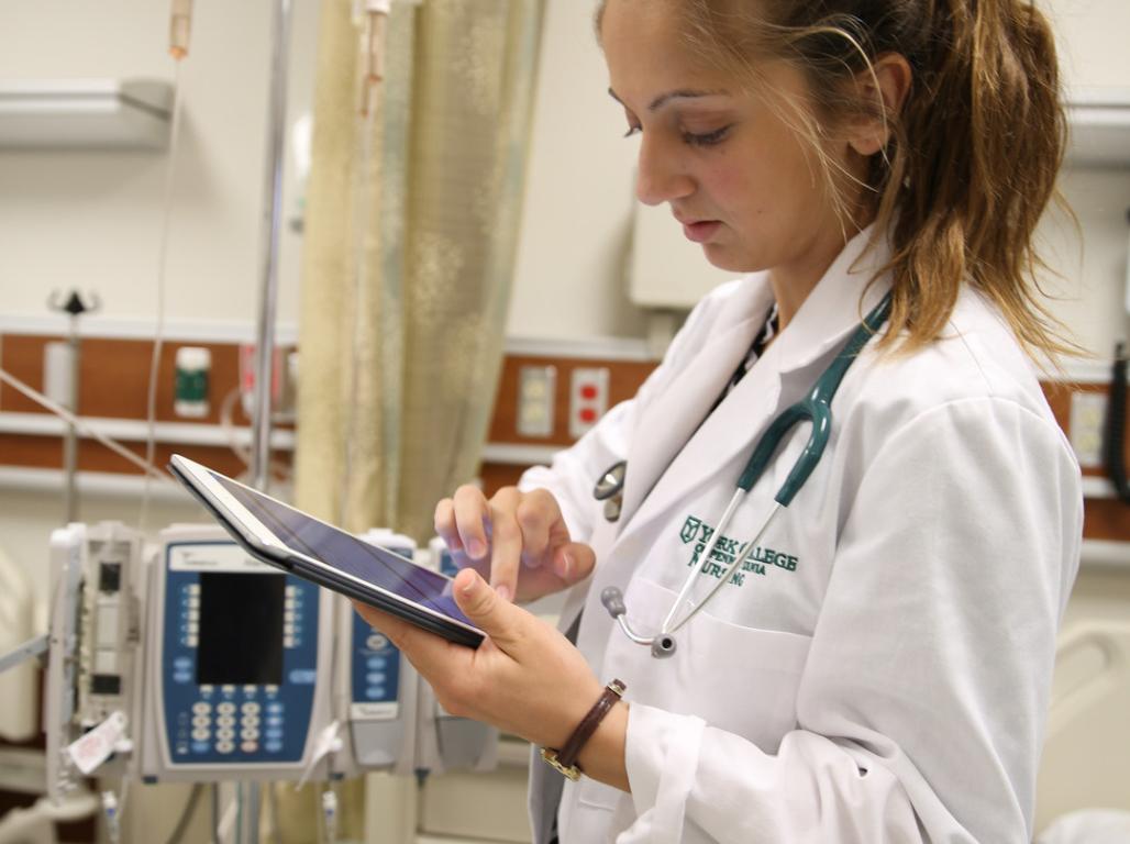 A nursing student holds a tablet in a medical setting