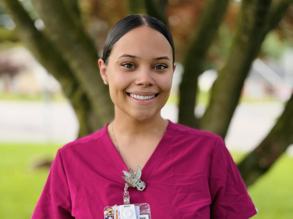 Nursing major Ke-lhja DeShields ‘27 smiles at the camera, wearing pink scrubs and an ID badge in an outdoor setting.