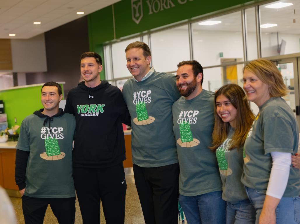 A group of people wearing YCPGives 2026 tee shirts pose for a photo in Johnson Dining Hall.