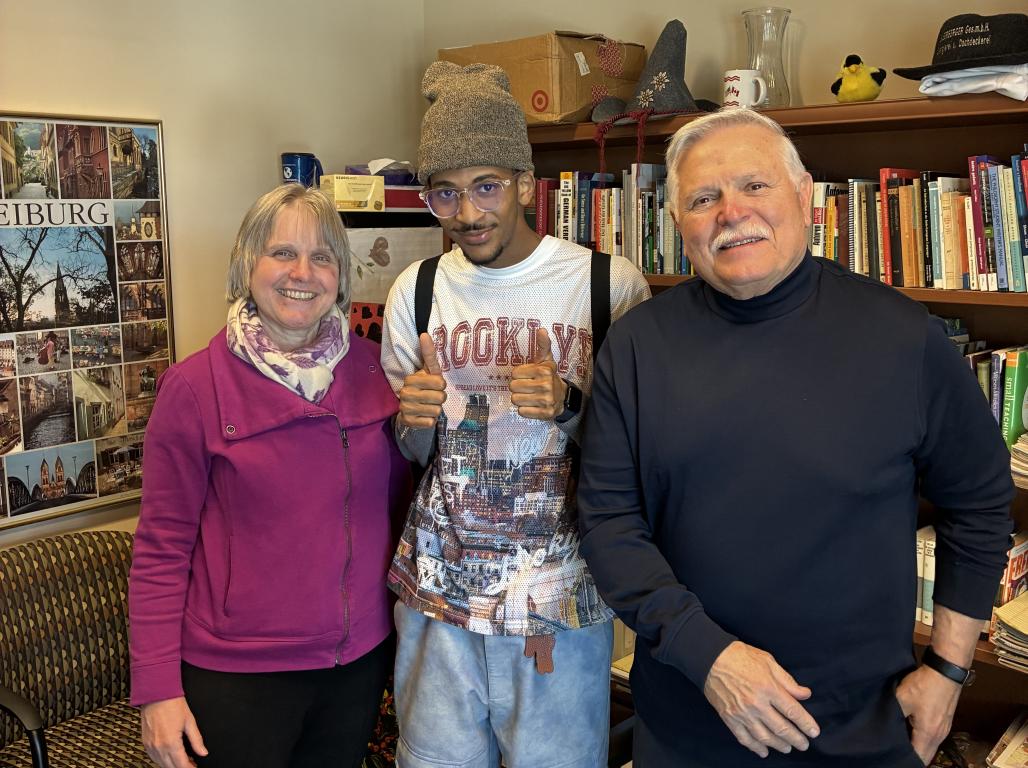 Three people standing in an office, smiling at the camera. A bookshelf is visible in the background.