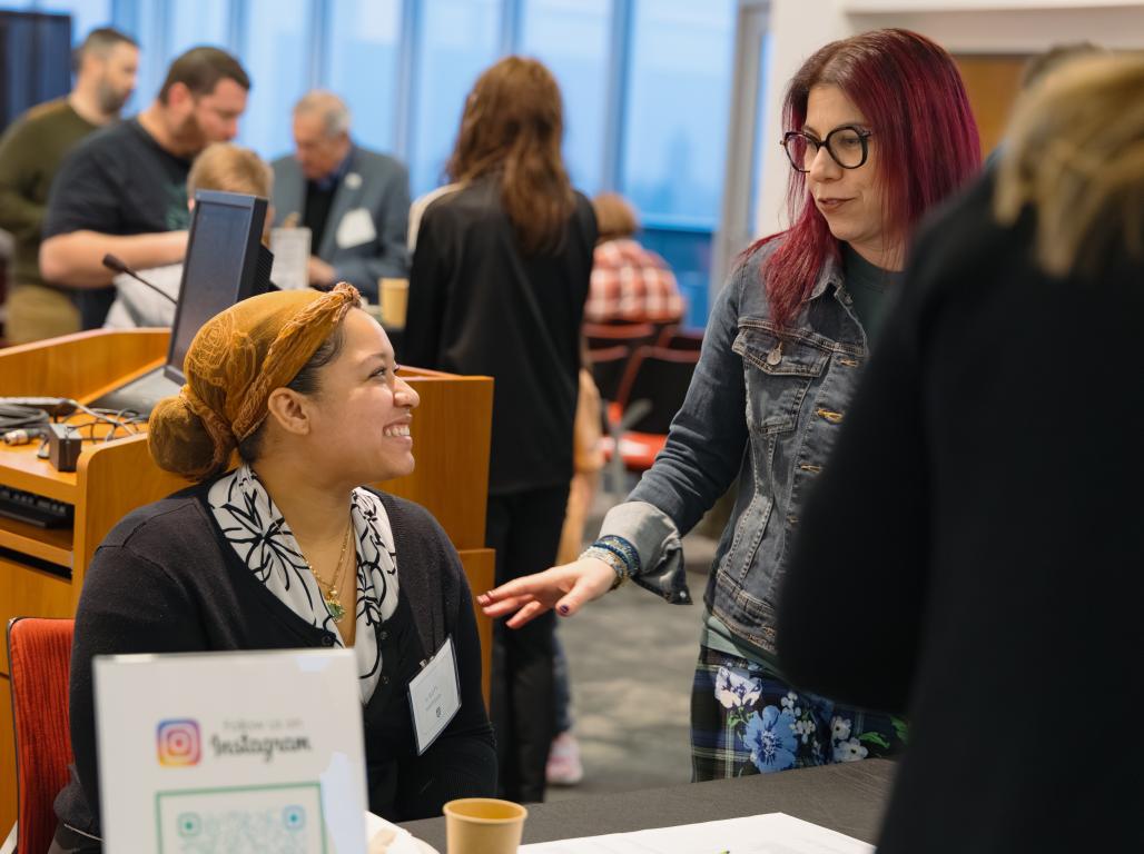 Two women smile at each other at a large gathering for the GCCI.