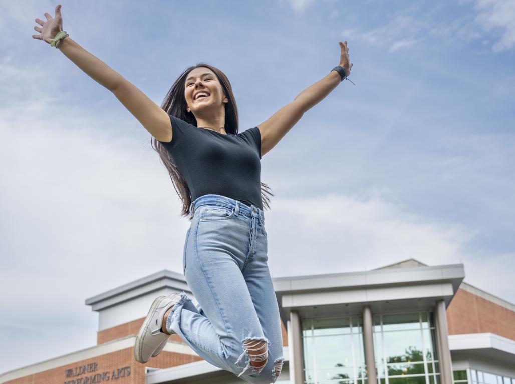 Megan Holtzinger '26 jumping joyfully with the WPAC building visible behind her.
